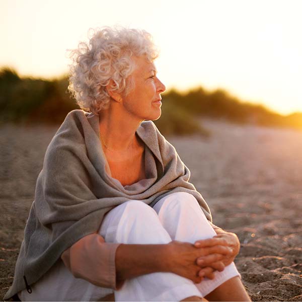Seniorin, die am Strand sitzend in den Sonnenuntergang schaut